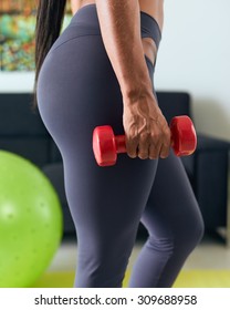 Young Adult African American Woman In Sports Clothing At Home, Doing Domestic Fitness And Training Biceps With Weight. Cropped View Of Hand And Legs