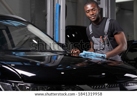 young adult afro american man cleaning car with microfiber cloth, car detailing or valeting concept