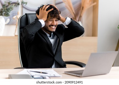 Young Adult Annoyed Businessman, CEO Or Manager From India, With A Beard, Experiencing Stress, Upset With Financial Losses, Bad News, Holds His Head With His Hands, Closes His Eyes