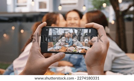 Young adult asia people hug cuddle kiss love care for mom taking photo selfie video on mobile phone camera at home picnic dining fun night party dine table. Relax older mum smile enjoy warm time meal.