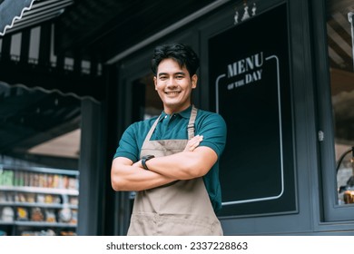 Young adult Asian business man crossing her arms in front of cafe restaurant while smiling. Happy and joyful barista of Coffee shop having arms crossed. High quality photo - Powered by Shutterstock