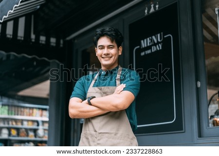 Young adult Asian business man crossing her arms in front of cafe restaurant while smiling. Happy and joyful barista of Coffee shop having arms crossed. High quality photo