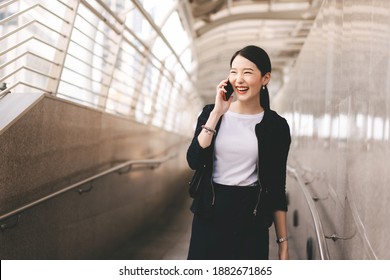 Young adult asian business single woman use mobile phone talking with friends. Her face has happy laugh. Fashionable look city lifestyle working people. Backgroud at outdside on day.