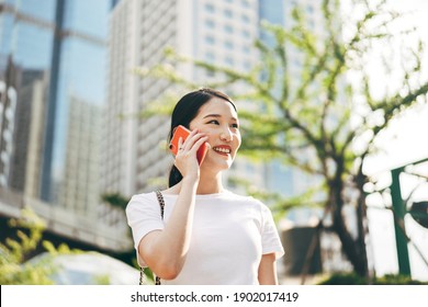 Young adult asian business single woman using mobile phone talking with friend. Happy face and laugh. City lifestyle working people. Backgroud at outdside on day.