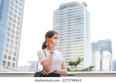 Young adult asian business single woman talking with smart phone. Wearing face mask new normal lifestyles. City lifestyle working people. Backgroud at outdside on day.