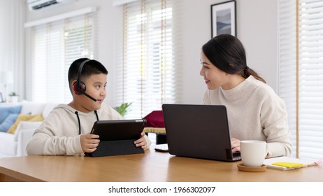 Young Adult Asian Mother And Kid Stay Home Work And Learning Online Remotely From Computer Tablet In Self Isolate From Lockdown Coronavirus Covid19 Social Distance. Homeschool Boy With Parent.