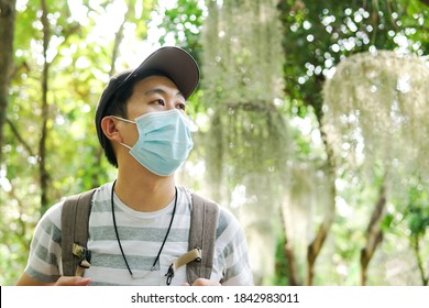 Young adult Asian travel backpacker wearing a face mask hiking in the forest. Millenial man wearing a cap walking in the nature during Covid-19 or Corona Virus pandemic. - Powered by Shutterstock