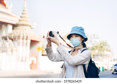 Young adult asian woman backpack traveller wear face mask for corona virus or covid-19 Female people using camera for photography. New normal city lifestyle concept. - Powered by Shutterstock