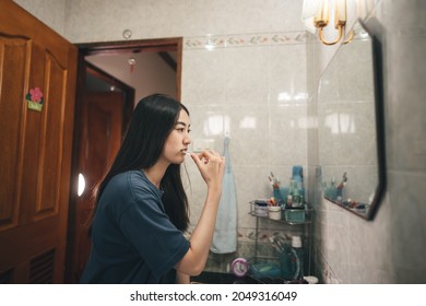 Young Adult Asian Woman Brushing Teeth In Font Of Bathroom Mirror. Routine Lifestyle In Morning At Home Concept.