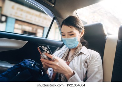 Young Adult Asian Woman With Face Mask For Public Health In Car. Using Mobile Phone Application For Call Taxi Driver And Map Destination. Single People Transport In City Travel Lifestyle Concept.