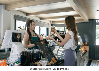 young adult Asian woman, owner of a coffee shop or a skilled barista, stands beside a beautifully arranged display of coffee mugs for her valued customers. - Powered by Shutterstock