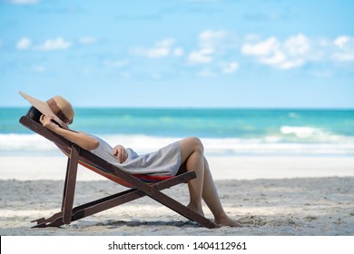 Young adult asian woman tourist in casual wear sleeping nap on beach sun bed on tropical island sand beach in summer day holidays vacation travel trip with blurred blue sea, beach and sky backgrounds.