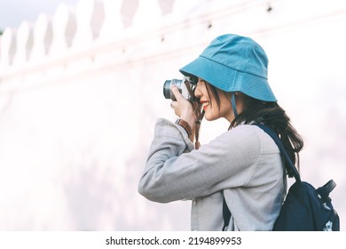 Young Adult Asian Woman Traveller Wear Blue Hat And Backpack Using Camera For Photo Tour. People Traveling In City Lifestyle On Day. Staycation Summer Trip Concept.