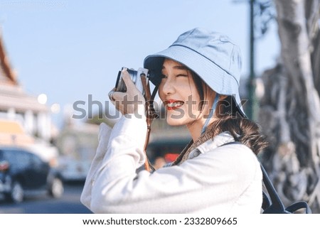 Young adult asian woman traveller wear blue hat and backpack using camera for photo tour. People traveling in city lifestyle on day. Staycation summer trip concept.