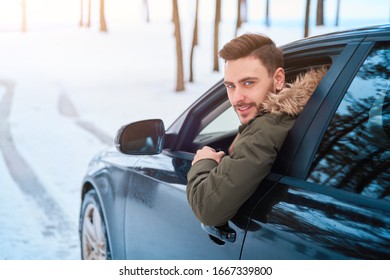 Young Adult Attractive Caucasian Man Sits At The Wheel Of His Car Sunny Winter Day. Wintertime Road Trip. Happy Smiling Hipster Guy Sitting In Car And Looking Window. Portrait Positive Driver 