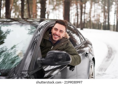 Young adult attractive Caucasian man sits at the wheel of his car sunny winter day. Wintertime road trip. Happy smiling hipster guy sitting in car and looking window. Portrait Positive driver 