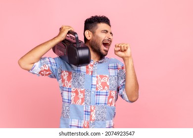 Young Adult Bearded Crazy Man Holding Tape Recorder Over Shoulder, Listening Music, Singing With Conspicuous Microphone, Wearing Blue Shirt. Indoor Studio Shot Isolated On Pink Background.