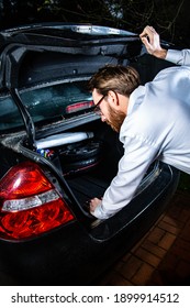 Young Adult, Bearded Man Looking Into A Car Trunk, A Boot At Night. 