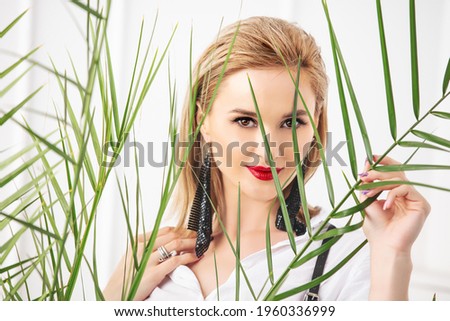 Young adult beautiful female model, portrait with makeup through tropical leaves on a white background