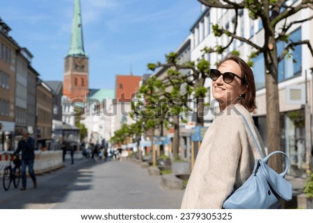Young adult beautiful happy woman walking by pedestrain shopping Wide street in Lübeck city with Jakobi gothic church in old town center. UNESCO heritage city altstatd in Germany travel destination.