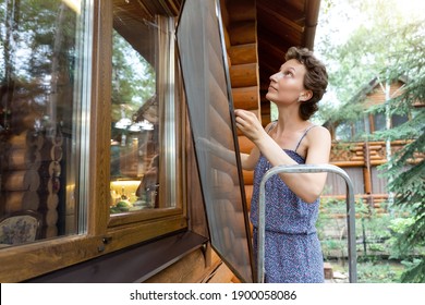 Young adult beautiful slim sporty caucasian woman stand on metal ladder and installing window mosquito insect fly screen protection. Female person housewife attach plastic mesh home wall summer day