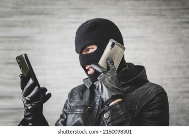 Young adult in black clothes with hidden face. Ill-intended fraudster uses mobile. Fraudster calls. Mobile racket. Hacker hijacks by phone. Cellphone account fraud. Scam