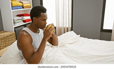 A young adult black man drinking coffee in a cozy, well-lit bedroom interior, exhibiting a relaxed morning routine - Powered by Shutterstock