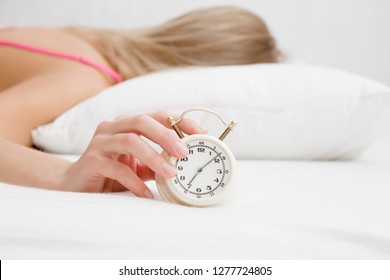 Young Adult Blonde Woman Sleeping On White Pillow In Bed. Hand Turns Off Alarm Clock In Morning. Not Getting Enough Sleep. Can't Wake Up.