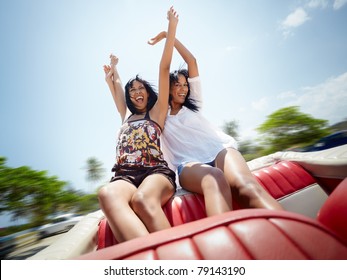 young adult brunette twin women sitting in convertible red car and laughing. Horizontal shape, front view, copy space