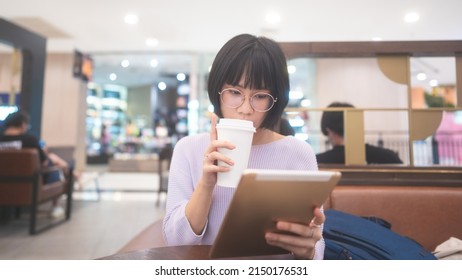 Young Adult Business Asian Woman Sipping Coffee And Using Tablet For Online Internet At Indoor Public Cafe On Day. Single People Lifestyle In City Concept.