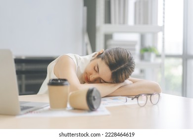 Young adult business asian woman fatique and sleep on table at office. Businesswoman tired from working overtime. Blur foreground with coffee cup. Window light background on day. - Powered by Shutterstock