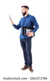 Young Adult Business Man Holding Laptop And Tablet Under Arm Checking Cell Phone Signal. Full Body Isolated On White Background.