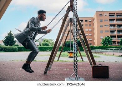 Young adult business man sitting alone in a playground swinging on a seesaw enjoying freedom focused on success