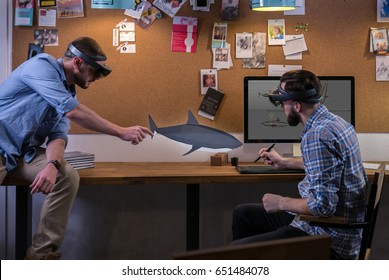 Young adult Caucasian colleagues using holographic augmented reality glasses together, discussing shark model hologram. Game development