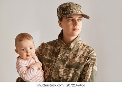 Young Adult Caucasian Female Soldier With Her Little Cute Infant Daughter In Hands, Looking Away With Serious Sad Facial Expression, Returning Home After War Or Army.