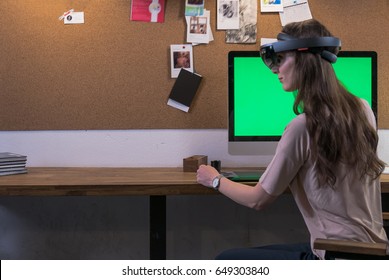 Young adult Caucasian female using holographic augmented reality glasses, creating a model on a computer screen. Green screen chroma key