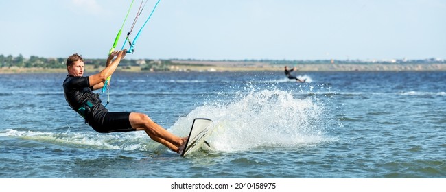 Young adult caucasian fit male person enjoy riding kite surf board in sun uv protection suit on bright sunny day against blue sky at sea or ocean shore. Watersport adrenaline fun adventure acitivity