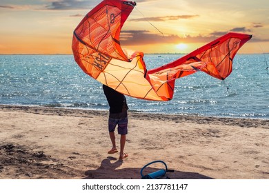 Young adult caucasian fit male person enjoy prepare kite surf board in sun uv protection suit on bright sunny day against blue sky at sea or ocean shore. Watersport adrenaline fun adventure acitivity