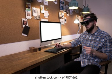 Young adult Caucasian male using holographic augmented reality glasses, creating a model on a computer screen