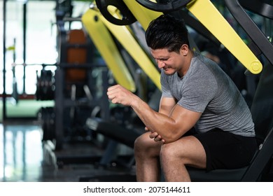 Young Adult Caucasian Men Feeling Painful From Elbow Muscle Injury After Workout With Weight Lifting Machine Inside Of Fitness Gym. Muscle Injured From Workout Or Exercise For Over Weight Training.