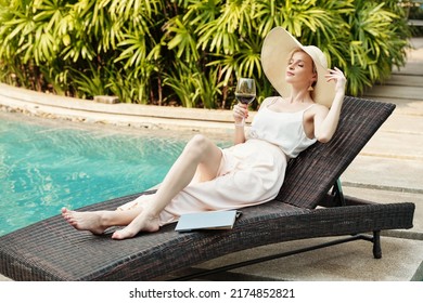 Young adult Caucasian woman relaxing on deck chair at poolside with glass of red wine on summer vacation day - Powered by Shutterstock