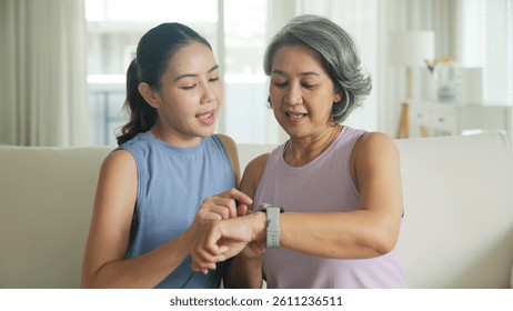 Young adult child give gift AI smart watch IOT app to mature middle age old mum. Love health care older mom asia elder people sit at home sofa happy family wear wrist trace help protect aging life.