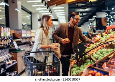 Young adult couple choosing some fresh fruits in grocery store, with shopping trolley beside them - Powered by Shutterstock