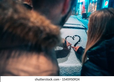 Young Adult Couple Draws A Heart On Snow Covered Car