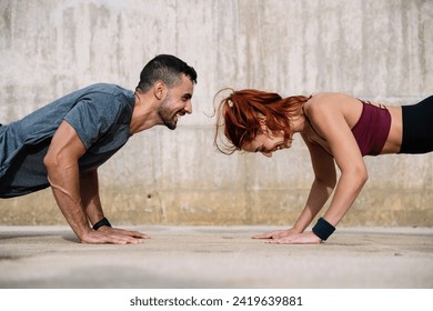 Young adult couple exercising in the floor face to face outside. Joyful athletic male and female doing push ups in the street in sportswear training workout outside.  - Powered by Shutterstock