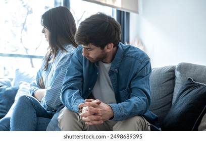 Young adult couple at home after discussion upset with man asking sorry to woman sitting and ignoring him looking outside the window. Relationship break up divorce concept moment. Tension financial - Powered by Shutterstock