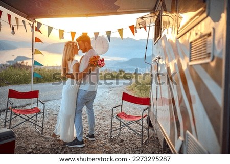 young adult couple hugging, holding each other in arms,  looking each other in love, in front of a camper outdoor at the sunset and beautiful view