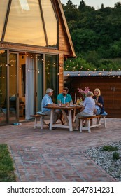 Young Adult Couple Sitting With Senior Couple And Little Girl At The Dining Table In The Backyard And Having Dinner