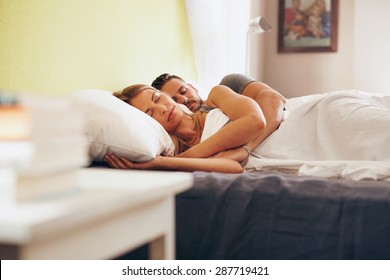 Young adult couple sleeping peacefully on the bed in bedroom. Young man embracing woman while lying asleep in bed.