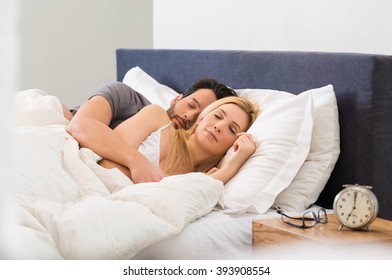 Young adult couple sleeping peacefully on the bed in bedroom. Young man embracing woman while lying asleep. Loving couple sleeping lying in bed at home.